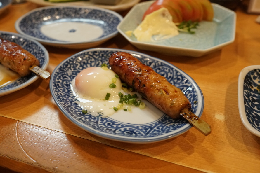 Chicken sausage skewer with soft egg, topped with chopped spring onions